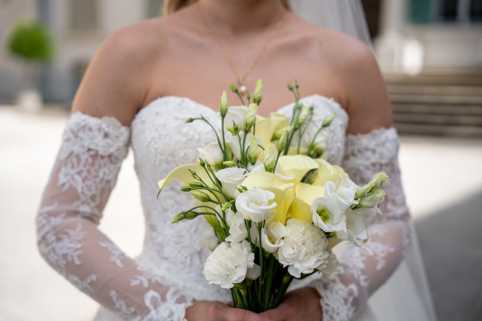 Brautstrauß mit weißen und gelben Blüten vor dem Spitzenkleid