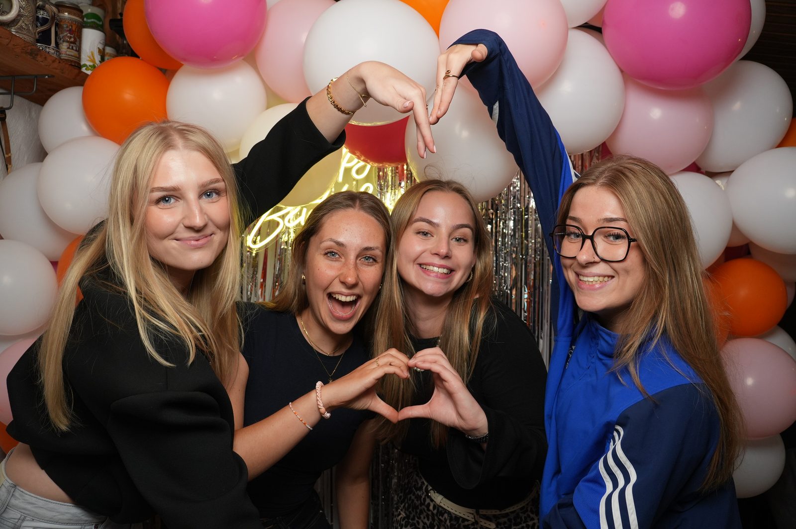 Fotobox: Freundinnen formen Herzen vor einer bunten Ballonwand