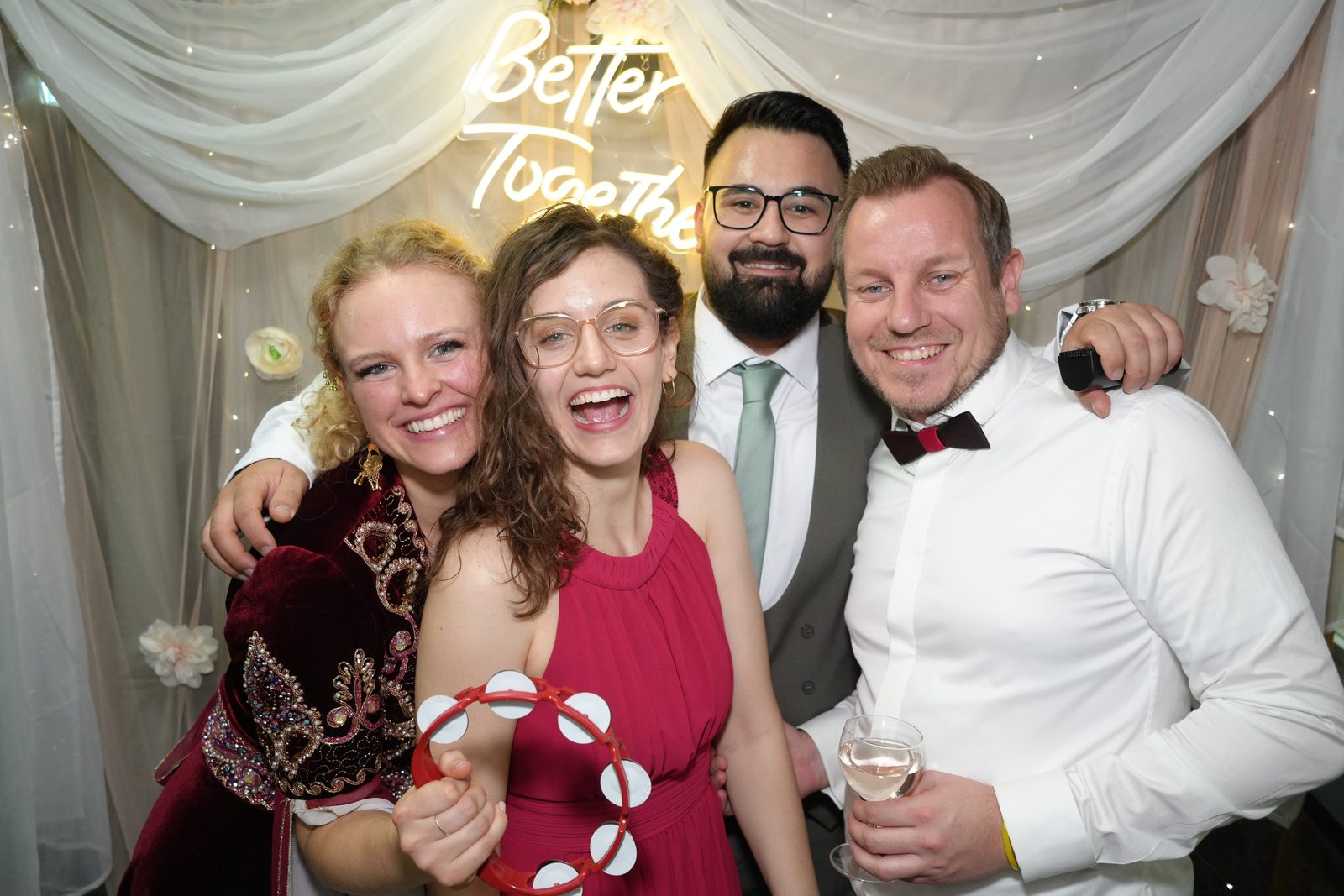 Fotobox: Gäste lachen gemeinsam vor Vorhang und Neon-Schrift