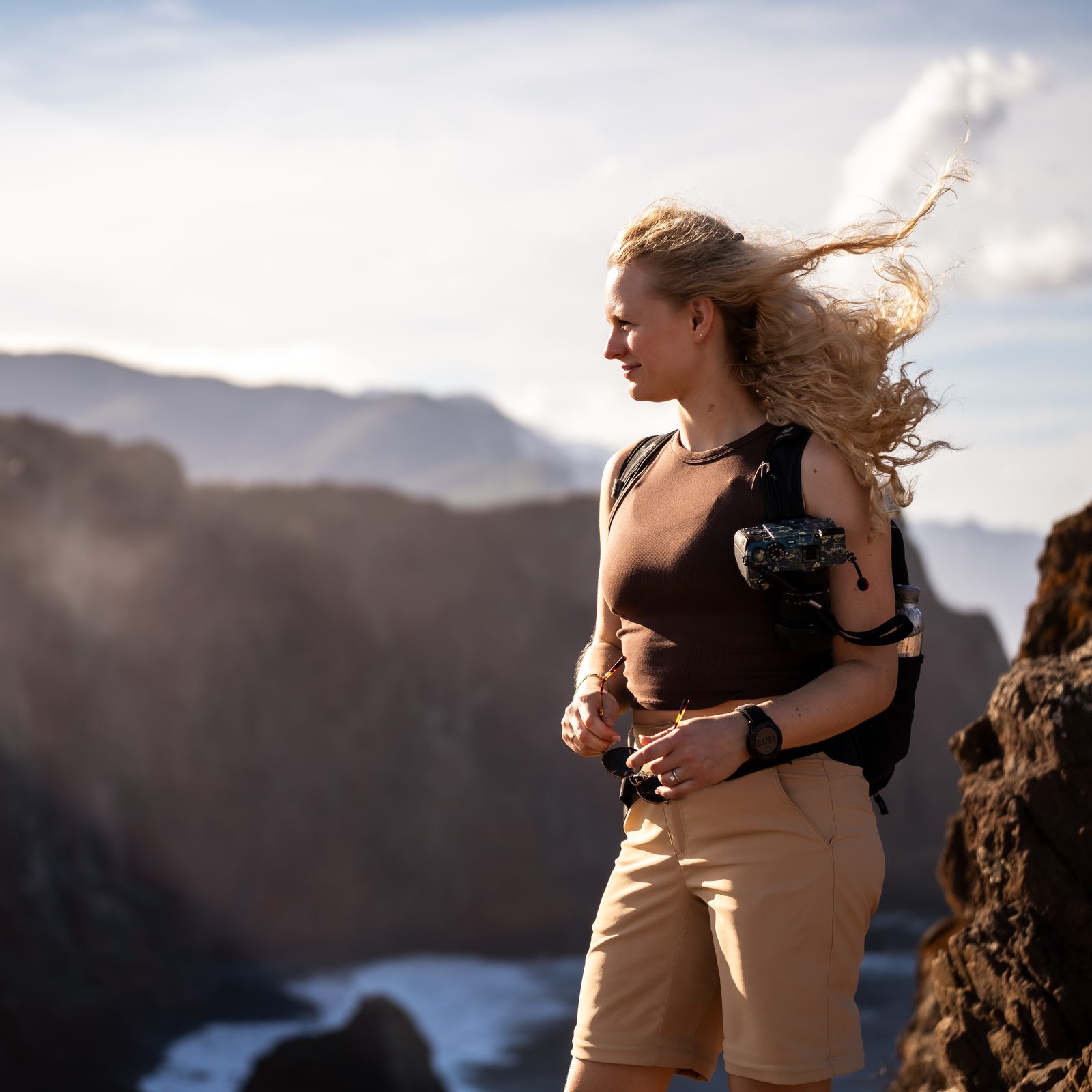 Vanessa Tuncer mit Kamera an einer Steilküste, der Wind weht durch ihre Haare